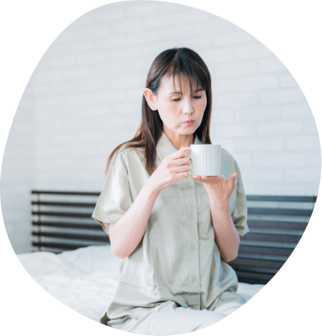 Woman holding white coffee mug while sitting on bed
