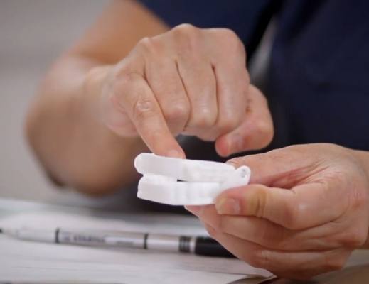 Person holding white oral appliance for obstructive sleep apnea treatment