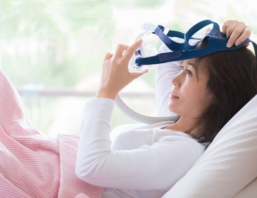 Woman in bed putting C P A P mask over her face