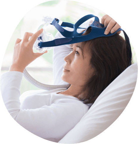 Woman in bed placing a C P A P mask over her face
