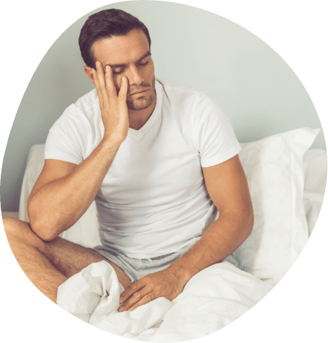 Frustrated man sitting up in bed and resting his face in his hand