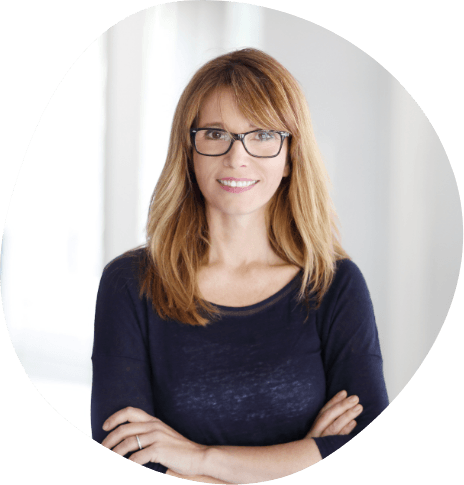 Blonde woman with glasses standing and smiling with arms crossed