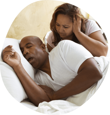 Frustrated woman in bed covering her ears while glaring at snoring man next to her