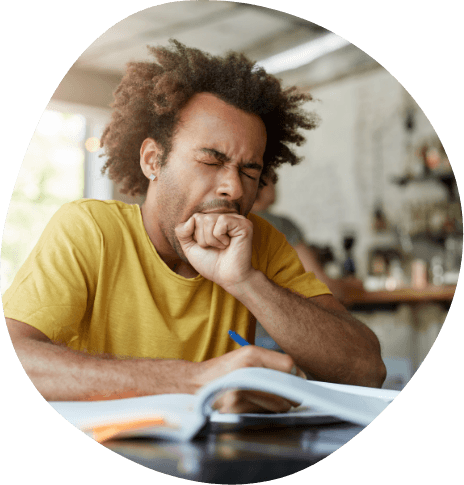 Man yawning while sitting at desk with book open