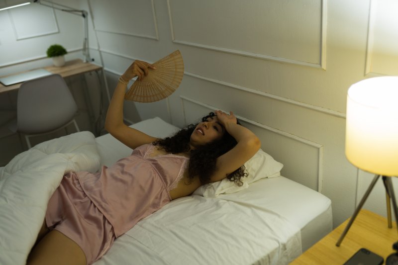 woman lying in bed fanning herself because it is hot